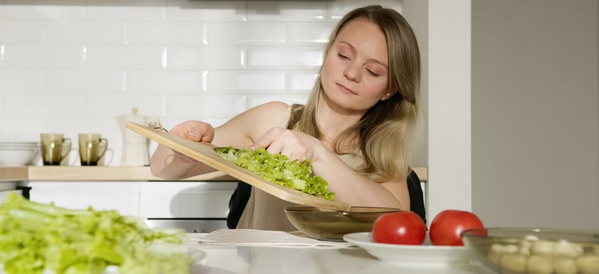 A woman preparing a fresh salad with lettuce and tomatoes in a modern kitchen.