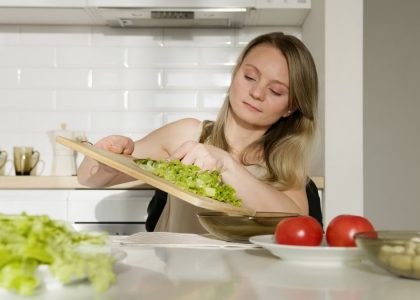 A woman preparing a fresh salad with lettuce and tomatoes in a modern kitchen.