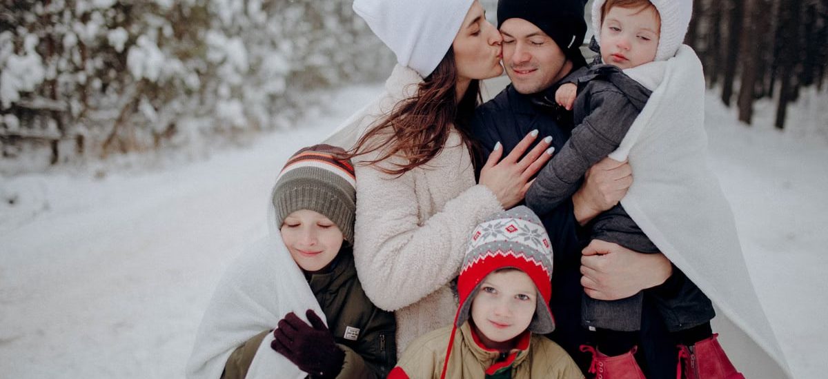 A joyful family enjoying a snowy day in a forest, wrapped in warm clothing.