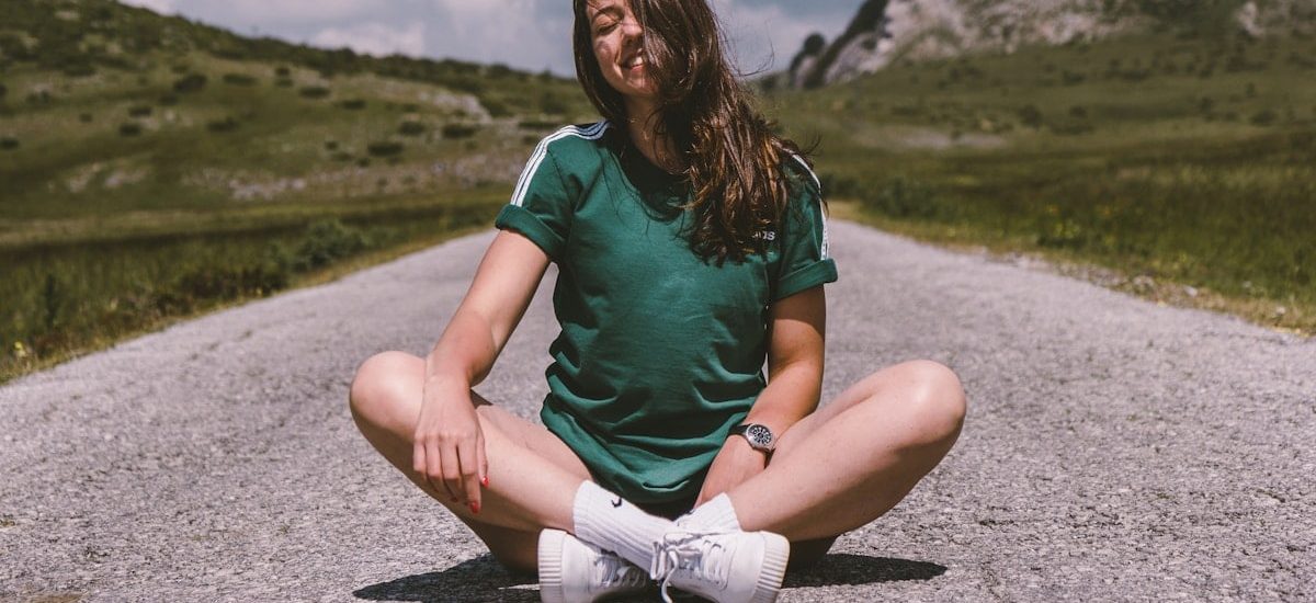A girl sits on a road in the middle of nowhere, smiling while enjoying the warmth of the sun