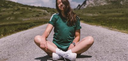 A girl sits on a road in the middle of nowhere, smiling while enjoying the warmth of the sun