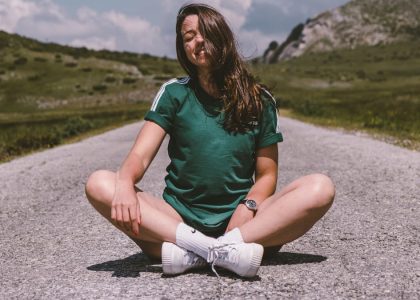 A girl sits on a road in the middle of nowhere, smiling while enjoying the warmth of the sun
